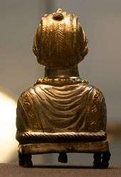 The golden back of a statue of a lady made from metal standing on dumpy feet