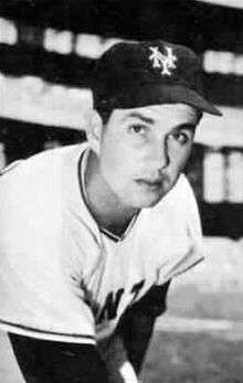 A black and white photograph of a man in a white baseball jersey and dark cap with "NY" on the front leaning forward