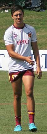 A man in a white shirt and maroon shorts stands on grass