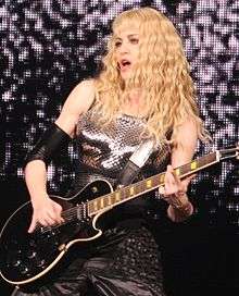 Madonna playing a guitar onstage, while looking to her right.