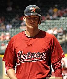 A smiling young man wearing a red baseball jersey with "Astros" across the chest and a black batting helmet with an incomplete red star on the face