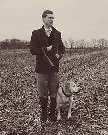 A hunter poses with a Lab in a snowy corn field.