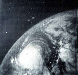 Monochrome satellite image of a tropical cyclone. The tropical cyclone, located at bottom-center, is round and has a distinct eye. Due to the angle of the camera, the curvature of the Earth is clearly visible.