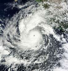 A mature hurricane, featuring a circular cloud mass with a small, well-defined eye in the center, approaches Mexico from the southwest.