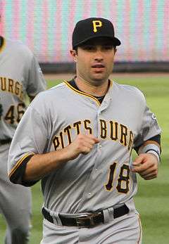 A light-skinned man in a gray baseball uniform with "PITTSBURGH" on the chest and a black baseball cap with "P" in yellow on it jogs towards the camera.