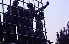 Close-up of sculpted human figures reaching through the fence