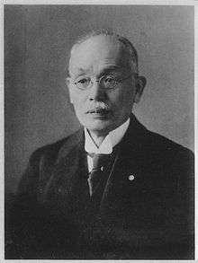A black-and-white photograph of a Japanese man looking left