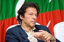 Imran Khan, seated in front of a Pakistani flag