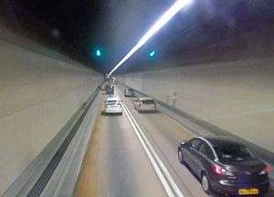 A two-lane road in a tunnel with plain brown sides and one overhead light strip.