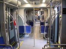 Interior of a light rail vehicle with blue seats, gray walls and silver pedestrian supports.