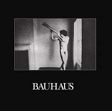 The album cover has a black background with a square in the middle featuring a black-and-white image of a naked man posing with a metal object. Below this is captioned "Bauhaus" in white text.