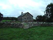 A very small stone church with lancet windows and a single west bellcote