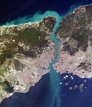 Satellite image showing a thin piece of land, densely populated on the south, bisected by a waterway