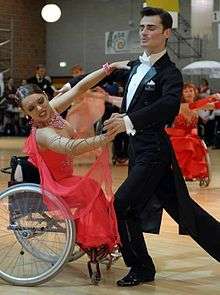 A wheelchair-bound woman in a ball gown dancing with a man in a tuxedo