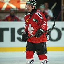 A Caucasian male ice hockey player shown from the knees up. He is wearing a red and white sweater with a dark helmet.