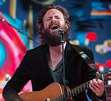 Josh Tillman plays guitar standing up and sings into a microphone