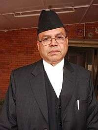 A bespectacled Jhala Nath Khanal, wearing a hat and a dark suit
