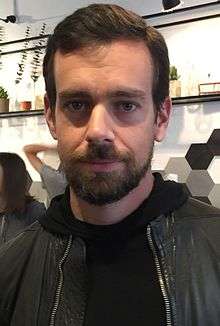 image of Jack Dorsey at a London cafe in November 2014, smiling with his mouth closed, and wearing a dark upper garment and jacket