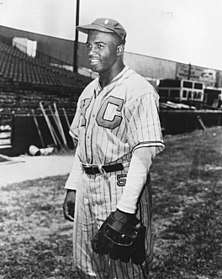 A black man wearing a pinstriped baseball uniform, hat, and glove