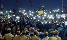 Students use their mobile phone flashlights to illuminate their protest after street lights are turned off by power company TNEB.