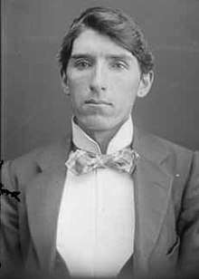 A black and white portrait photograph of a Caucasian man in his twenties wearing a suit and bowtie