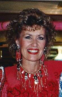 A woman with blonde hair wearing a red top and an elaborate gold necklace