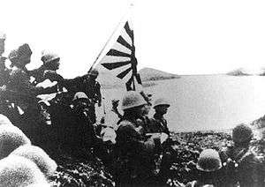 alt=Historic photograph of Japanese troops raising the Imperial battle flag on Kiska Island.