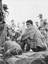 Japanese prisoners sitting, watched over by several Australians