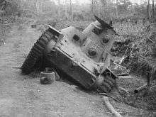 A small tank on a road, which is at a 45 degree angle due to one side being in the ditch beside the road