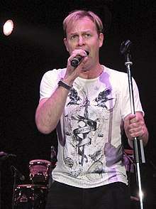 A Caucasian man performing on stage, wearing white T-shirt.