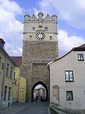  View of a street of old bauildings, the largest of which is a tall clock tower with an archway