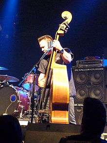 An upright bass player, Jimbo Wallace, performs onstage with his bass plugged into a large Gallien-Krueger bass stack and amplifier.