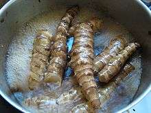 Several knobby elongated light brown tubers in pot with water