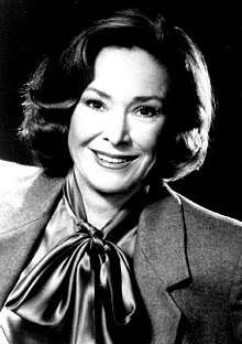 Black and white photo of a smiling woman about fifty years of age and wearing a jacket and tied-up scarf
