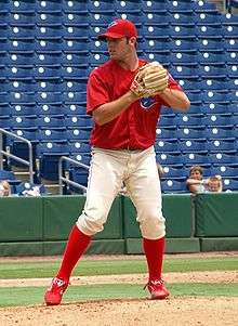 A young man wearing a red baseball jersey and cap and white baseball pants