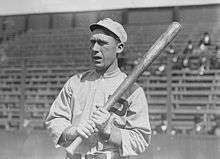 A black-and-white photograph of a man wearing a baseball sweater with a "P" over the left breast and a crownless baseball cap holding a baseball bat over his left shoulder