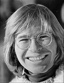 A man with long blond hair and glasses, smiling broadly
