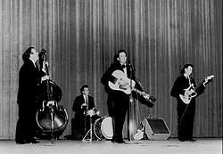 A group of men in dark suits playing various musical instruments on a stage
