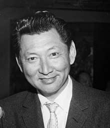 Black and white photograph showing head and shoulders of Johnny Kan, a restauranteur in Chinatown, San Francisco. Kan is wearing a dark suit with a light-colored tie.