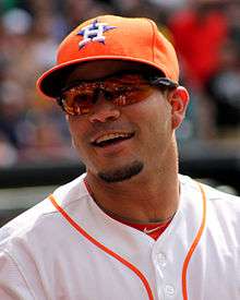 A man in a white baseball wearing and orange baseball cap with an "H-star" logo smiles.