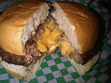 A beef burger oozing melted yellow cheese on a green and white checkered paper