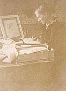 Julia writing letters at her desk in the drawing room of Talland House in 1892. On the desk is a drawing of her mother by Watts