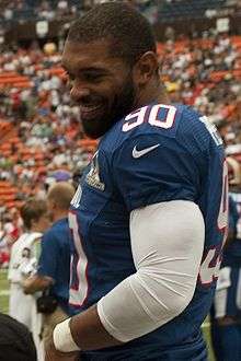 An American football player wearing a blue jersey with the number 90 while smiling.
