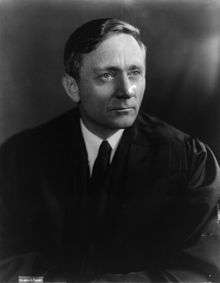 Black and white photograph; a man wearing a judge's robe looks off to the right