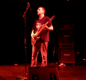 Justin Broadrick playing guitar on a red-tinted stage