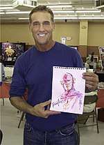 A man with dark hair, wearing blue T-shirt with jeans also holding an art piece of The Flash.