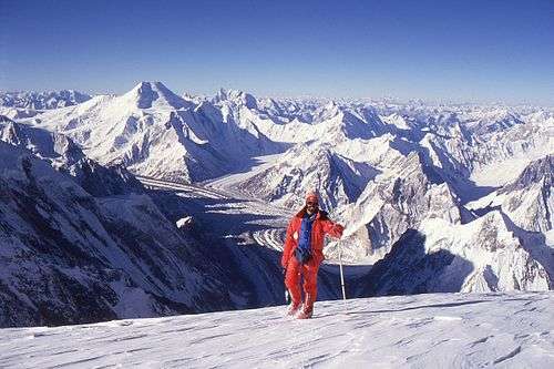 A climber stands in front of a vista of snow-covered mountains