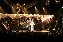 A band performs a song at a venue, behind the bright yellow stage lightings.