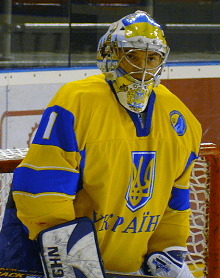 An ice hockey goaltender in full gear visible from the waist up looking towards the camera