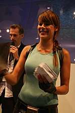 A half body picture of a brunette woman dressed in a light blue, sleeveless shirt holding a stack of papers.